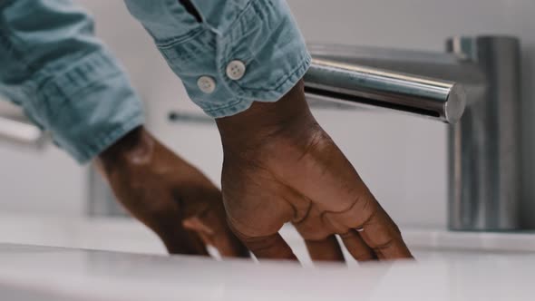 Unrecognizable African American Man Washes and Dries Male Hands Palms in Automatic Washbasin in