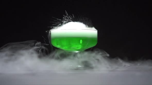 Green Liquid Boils Giving Off Smoke in a Glass Bowl on a Black Background