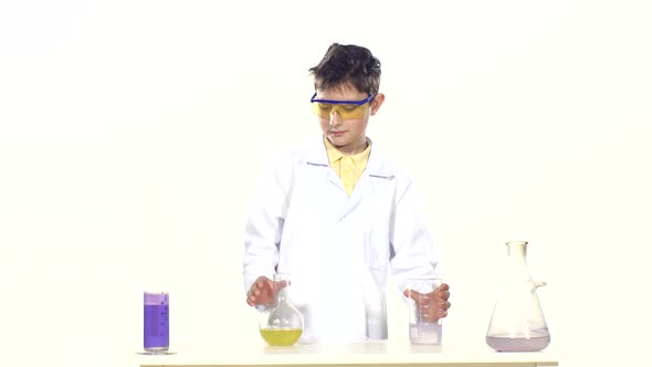 Scientist Boy in Uniform and Protective Glasses with Test Tubes, Evaluates, Standing By the Table