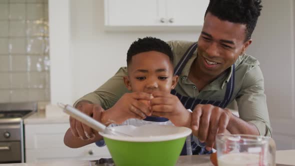 African american father teaching his son how to crack eggs while baking in the kitchen at home