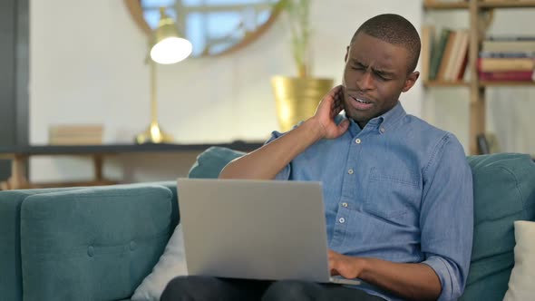 Laptop Work By Young African Man with Neck Pain on Sofa