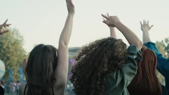 Rear view of friends dancing on music festival with hands up. Shot with RED helium camera in 8K.