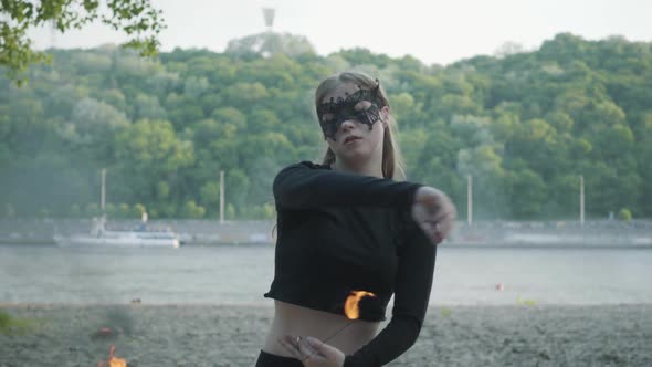 Confident Slim Woman in Mask Dancing, Performing a Show with Fireball Standing on the Riverbank