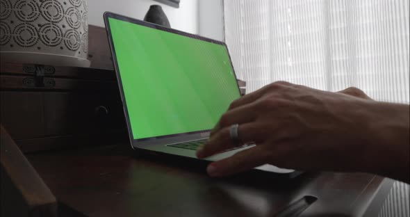 Employee working from home walks up to desk and opens laptop computer on desk. Computer screen green