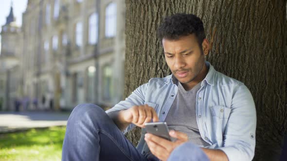 College Student Reading Newsfeed on Phone, Getting Disappointed With News, Upset