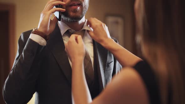 Young Man in Suit Talking on a Mobile Phone Woman Ties a Tie To a Man Business Trip Hotel Interior