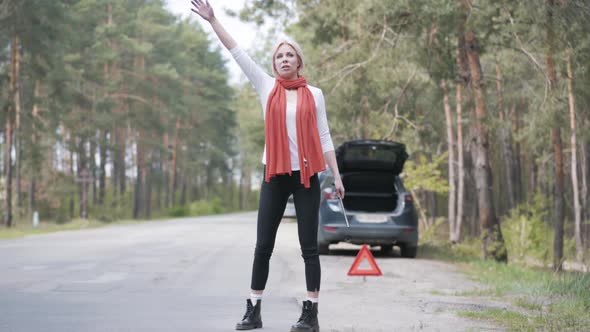 Desperate Blond Woman Hitchhiking on Suburban Road. Wide Shot Portrait of Stressed Caucasian Female