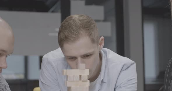 Closeup Portrait of Young Handsome Concentrated Man Playing Jenga with Friends