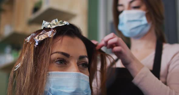 Female hairdresser dying hair of female customer wearing face mask at hair salon