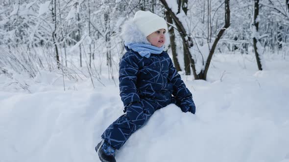 Child Sitting on the Snow in the Woods in the Winter