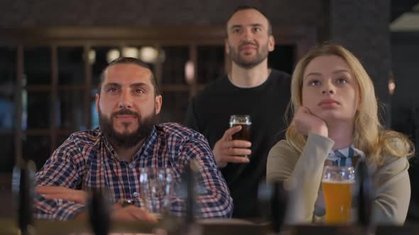 Group of Friends Watching Sports Match Sitting in Pub at Bar Counter