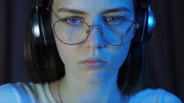 Closeup Portrait of Teenage Girl with Glasses and Wireless Headphones Looks at the Monitor