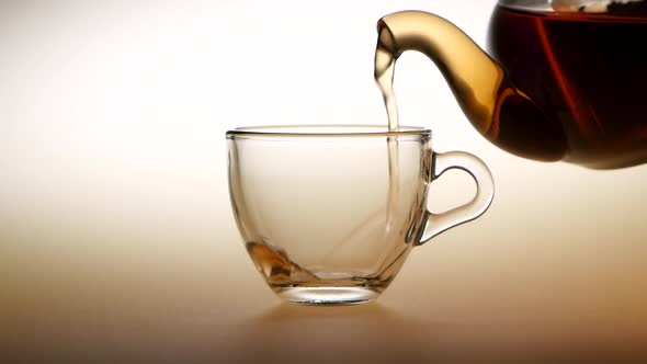 Tea Is Poured From Teapot Into Glass Cup. Slow Motion