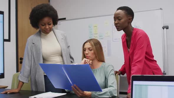 Three diverse businesswomen in discussion looking at paperwork in an office