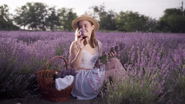 A Young Beautiful Caucasian Lady Sits on a Lavender Field Holds a Bouquet of Fragrant Lavender