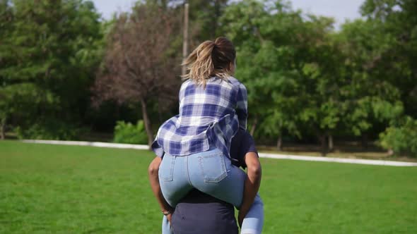 Back View of a Young African Guy Piggybacking His Caucasian Happy Girlfriend in a Sunny Park