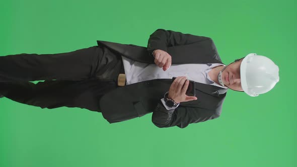 Asian Chief Engineer In The Hard Hat Use Mobile Phone While Walking On Green Screen Chroma Key