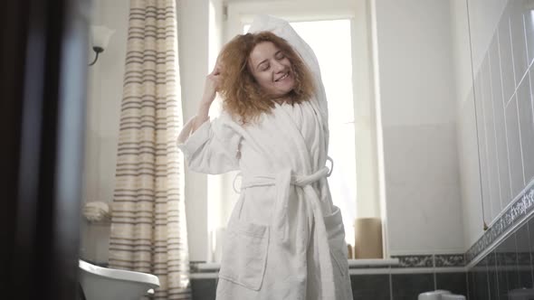 Portrait of Positive Redhead Woman in Bathrobe Stretching in the Morning in Bathroom