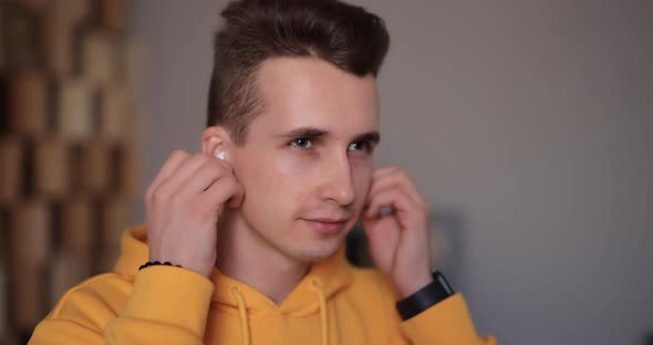 Man in Yellow Hoodie Puts on Wireless Earbuds Into His Ears at Home