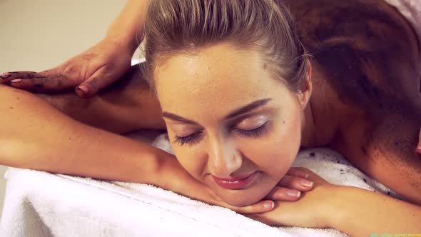 Relaxed Woman Lying on Spa Bed for Body Scrubbing Massage Using Traditional Herb