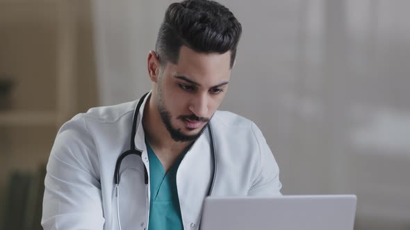 Concentrated Man Hispanic Doctor Physician Wear White Coat Use Computer Internet at Desk Type Recipe