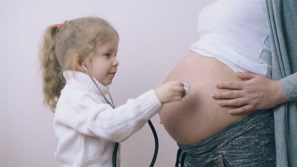 Girl with Stethoscope Touches Mommy Belly Listening To Baby