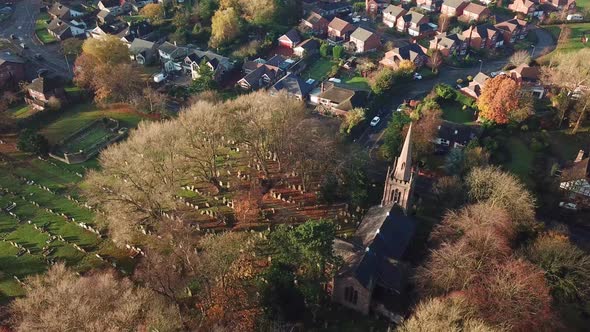 Aerial rotating shot above UK church in rural town. Autumn colours, houses & road.