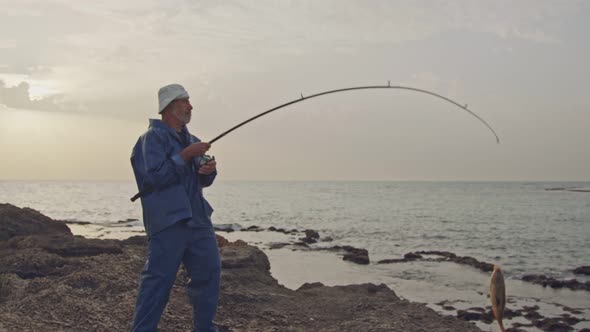 Old fisherman rising a large fish he caught on the beach