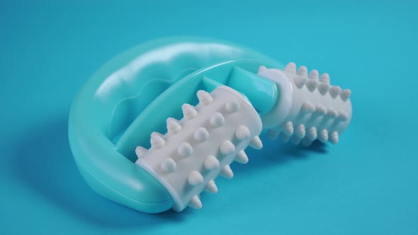 Manual turquoise plastic massager with white soft rollers and pimples 