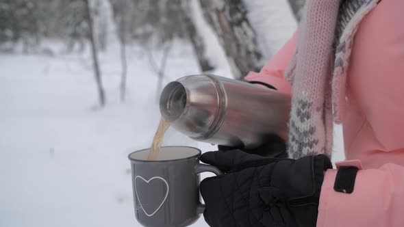 Woman Pouring Hot Tea From Thermos in Winter Day