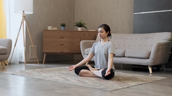 Athlete woman in sportwear practicing yoga at home in living room. Flexible Indian adult meditating