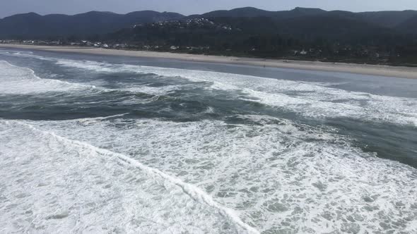Large emerald green waves break along a pristine Oregon coast beach, aerial