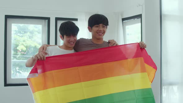 Portrait Young Asian Gay couple feeling happy showing rainbow flag at home.