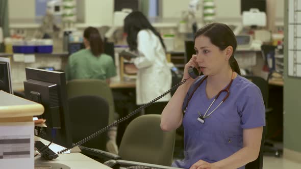 Nurses answers phone in busy nurse's station in a modern hospital.