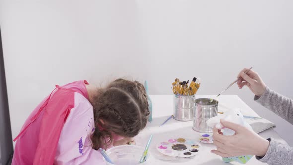 Little girl painting paper mache figurines with acrylic paint  for her homeschooling art project.