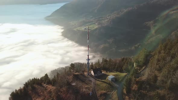 Network Base Station with large radio transmitter mast on the edge of a mountain slope above cloud c