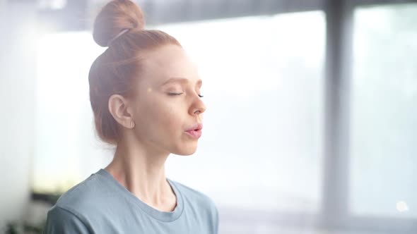 Close-up Face of Pretty Redhead Young Woman Doing Breathing Yogic Practices at Home Office.