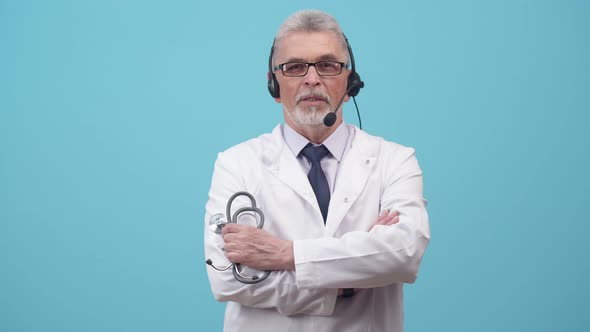 Man a Medical Gown Stands in a Headset and Talks Holding with Hand Stethoscope in the Studio