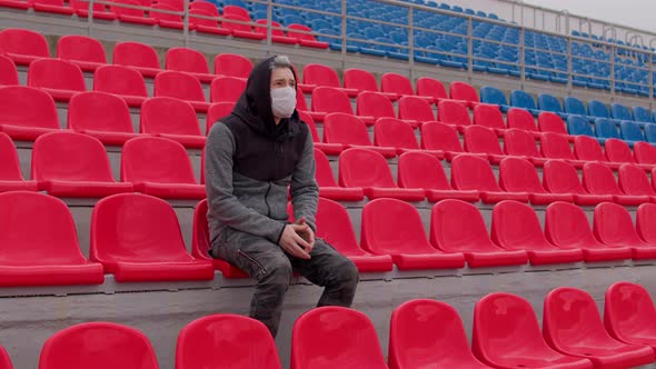 Young Man in Medical Mask Sitting on Stadium Bleachers Alone