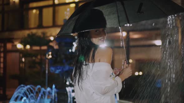 Wet Brunette Walks with Umbrella Under Rain and Smiles at Camera