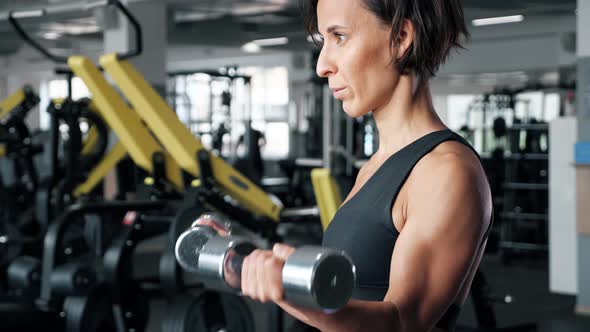 Sporty Mature Woman Is Making Biceps Exercise with Dumbbells in Gym