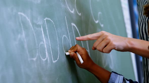 Teacher assisting schoolboy in writing alphabet on chalkboard