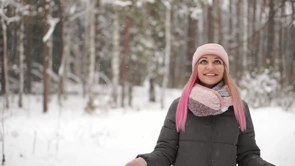 Woman in a Jacket and Hat in Slow Motion Looks at the Snow and Catches Snowflakes Smiling