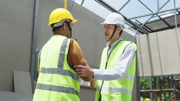 Asian structure engineer and worker wear safety hardhat making handshake on building working site.