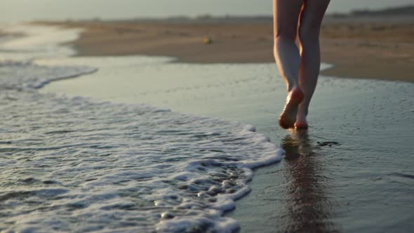 Women's bare feet walking along the seashore against the backdrop of sunset