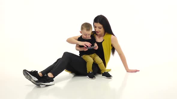 Woman Is Sitting on the Floor with Her Baby, She Is Stroking His Hair. White Background. Slow Motion