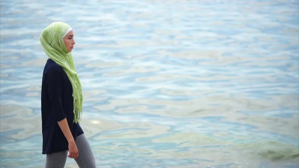 A Young Muslim Woman in a Veil Comes with a Pensive Look Along the Sea