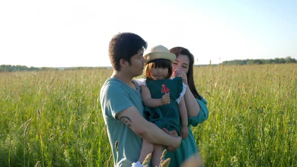 Korean Family with Their Daughter Go to the Field in the Grass at Sunset