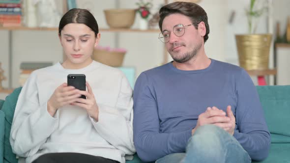 Hispanic Man Feeling Angry Near Female Partner Busy with Smartphone