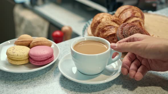 A woman's hand takes coffee from the bar counter of a coffee shop. Sweets on plates in a coffee shop